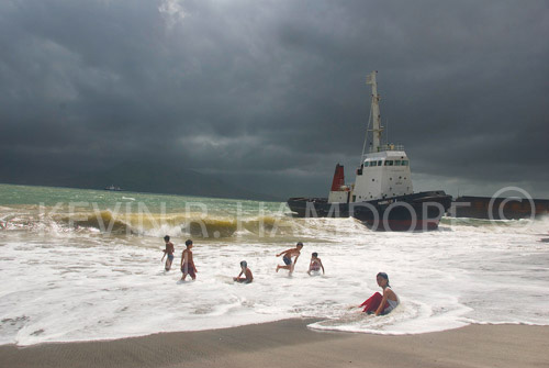 Monday, June 23rd 2008. Philippine President Arroyo declared schools closed in all areas effected by Typhoon Fengsen (Frank). School boys make the best of the situation on Kale Beach, Subic Bay. The grounded tug, “Pagbilao I” in the background.